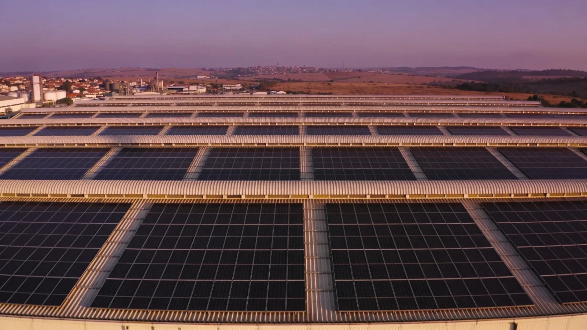 Cobertura de galpão industrial com fileiras de painéis solares ao entardecer.